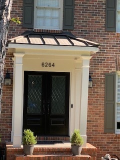 Black double door entry unit with decorative glass under a portico on a brick home — Westbrook Roofing and Remodeling