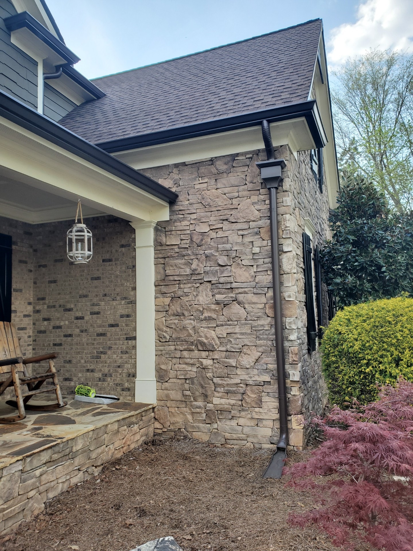 Seamless bronze downspout on stone home exterior — Westbrook Roofing and Remodeling