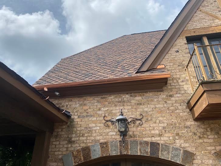 Copper seamless gutters installed on stone home with arched entry — Westbrook Roofing and Remodeling