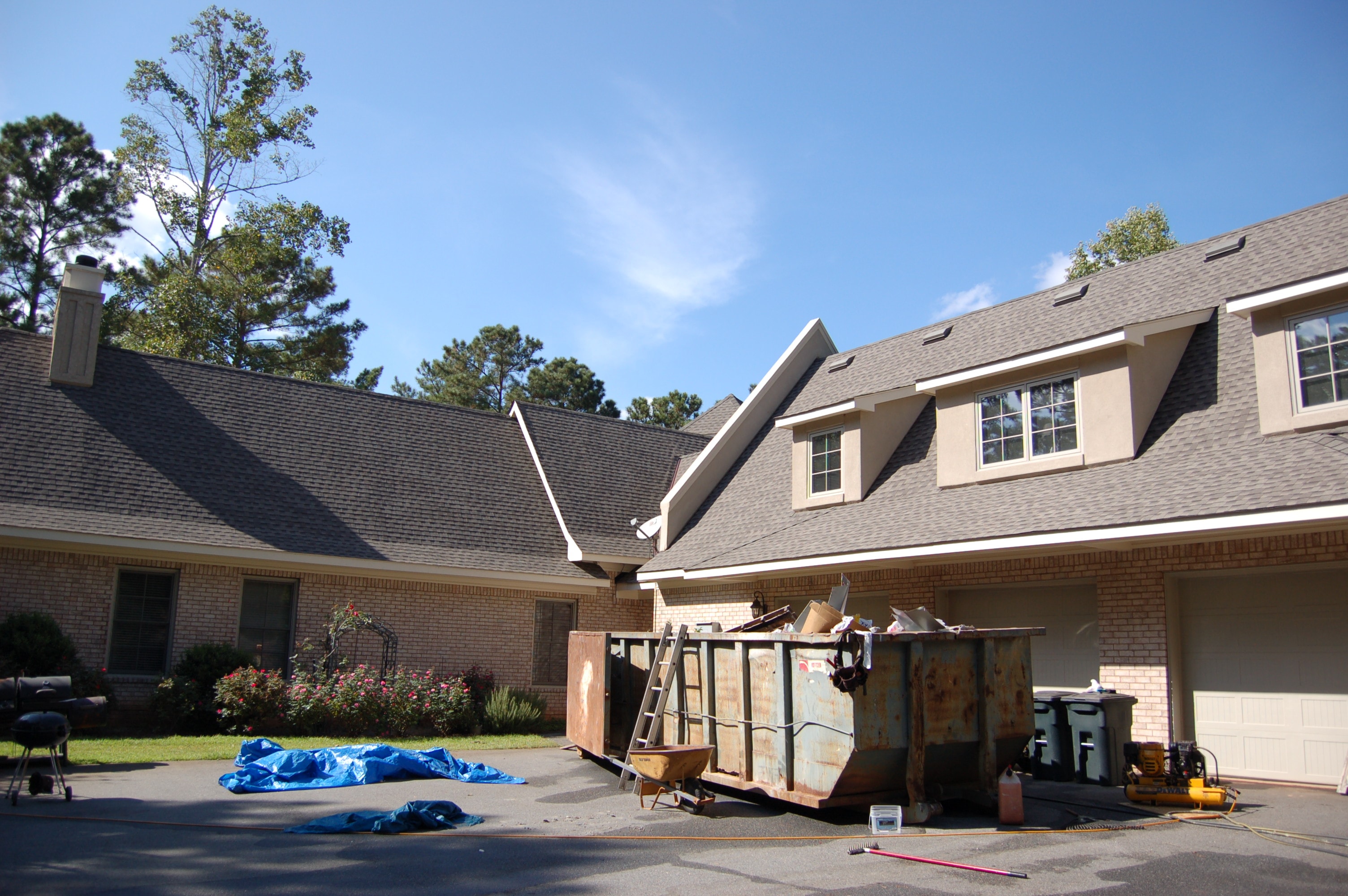 Roof tear-off in progress with debris dumpster on site