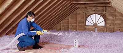 A man spraying foam on the inside of an attic.