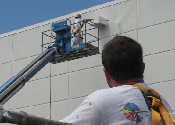 A man on a cherry picker painting the side of a building.