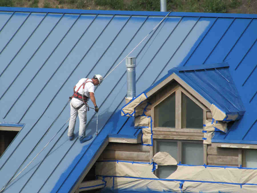 A man painting the roof of a house.